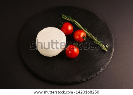 Salted soft cheese with cherry tomatoes on black background.