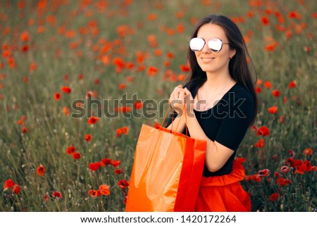 Fashion Woman With Shopping Bags Surrounded by Poppies. Fashonista posing in a field of flowers weaning big sunglasses
