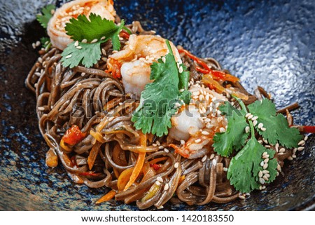 Close up on buckwheat noodles with shrimps served in black textured bowl. Thai cuisine. Seafood. Reaydy for eat. Picture for recipe. Copy space for design. Soba seafood
