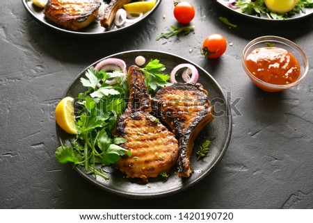 Tasty grilled pork steaks on plate over black stone table
