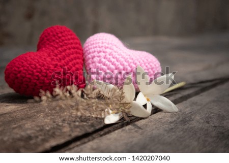 Red and pink knitting hearts with Millingtonia on the wooden rough table. Background of the rock wall. Sun light shines on the frame. Copy space for editing and text.