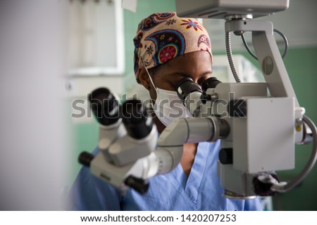 African Female doctor looking through Operating microscope equipment with face mask Cape Town South Africa.  Royalty-Free Stock Photo #1420207253