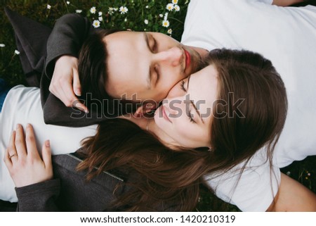 Young loving couple outdoors lying on grass, eyes closed, top down view. 