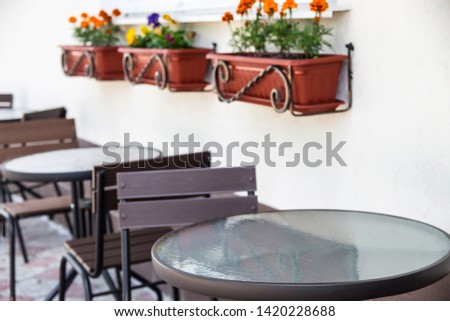 Glass and metal tables and chairs on a summer terrace cafe by the window with pots of flowers