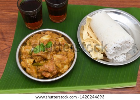 Popular South Indian steamed breakfast dish white Puttu or Pittu made of rice flour, grated coconut in bamboo mould with Malabar style Kozhi Pidi coconut chicken curry, black tea in Kerala, India. 
