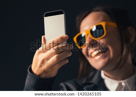 Cool businesswoman making selfie photo portrait with smartphone. Adult caucasian woman in elegant business suit wearing yellow sunglasses is posing in front of mobile phone camera.