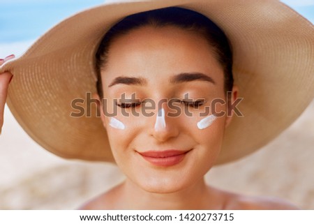 Beautiful woman applying cream sunscreen on tanned face. Sunscreen. Skin and body care. The girl uses a sunscreen for her skin. Portrait of a female holding suntan lotion and moisturizing sunscreen. Royalty-Free Stock Photo #1420273715