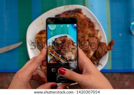 a woman's hand is holding a phone and taking pictures of food on the table, on screen of phone you can see the dishes
