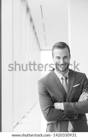 Black and white photograph or attractive businessman wearing a smart suit and standing in the office