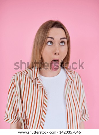 A young woman grimaces at the camera. The girl in the striped shirt on a pink background. Funny woman fooling around