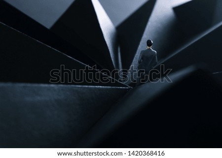 A picture of a miniature man stands in the geometric shapes looking forward .Concept of facing the unknown, taking a decision and finding solution.