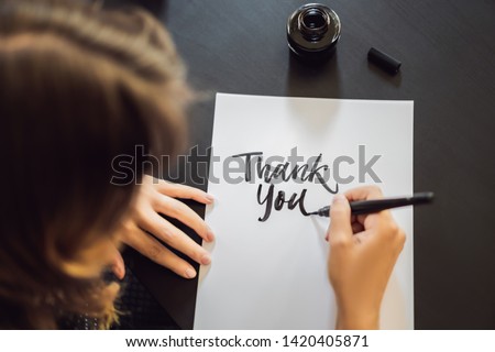 Thank you. Calligrapher Young Woman writes phrase on white paper. Inscribing ornamental decorated letters. Calligraphy, graphic design, lettering, handwriting, creation concept Royalty-Free Stock Photo #1420405871