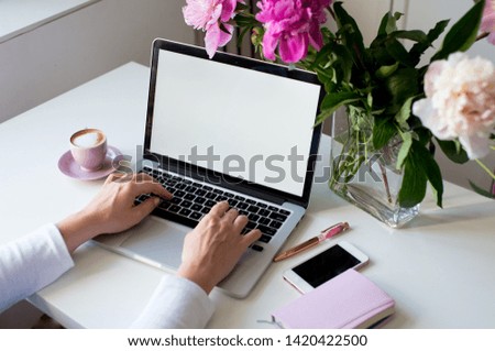 Female hands using laptop. Female office desk workspace homeoffice mock up with laptop, pink peony flowers bouquet, smartphone, pink accessories and pink cup of coffee. 