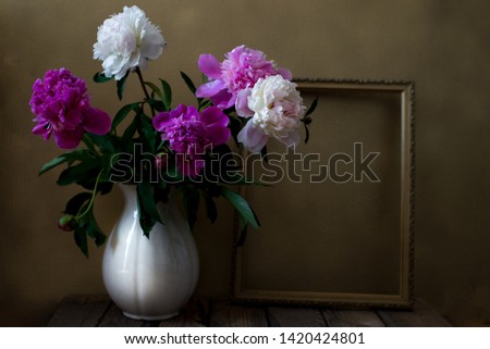 Still life with pink and white peonies in a white vase with empty frame on a gray background (textured for artistic effect). Copy space
