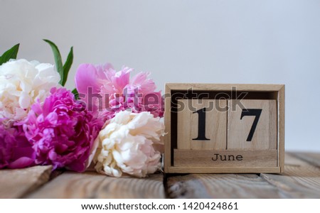 Wooden cubes calendar June 17. with pink and white peonies on a wooden table on a white background. Copy space 