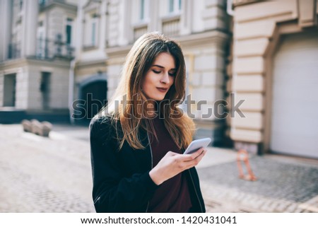 Attractive hipster girl outdoors  check mail by new cellular , woman sending text messages on modern mobile phone, female tourist searching news about places of  interest online walking on street