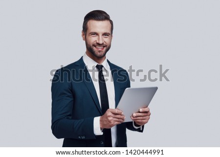Always ready to help. Handsome young man working using digital tablet while standing against grey background