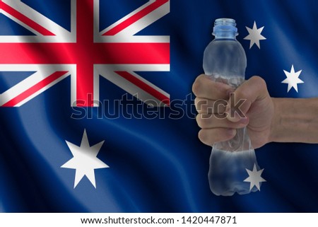 Concept of stopping plastic pollution. Ban disposable products. A hand squeezes a plastic bottle to protest the use of disposable plastic containers against the background of the flag of Australia
