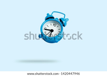 Flying blue alarm clock on a blue background. Levitation Royalty-Free Stock Photo #1420447946