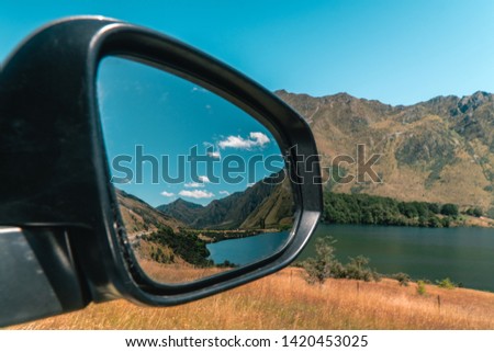 Mirror reflection of beautiful green grass and mountains in car wing mirror. Open window, driving through nature in New Zealand. Travel, reflect, mirror, background, outdoor concepts.