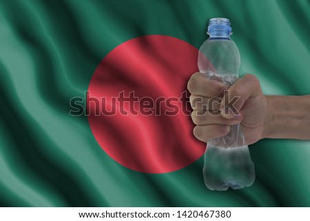 Concept of stopping plastic pollution. Ban disposable products. A hand squeezes a plastic bottle to protest the use of disposable plastic containers against the background of the flag of Bangladesh