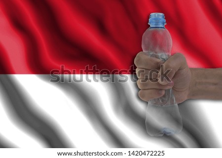 Concept of stopping plastic pollution. Ban disposable products. A hand squeezes a plastic bottle to protest the use of disposable plastic containers against the background of the flag of Monaco