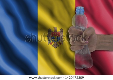 Concept of stopping plastic pollution. Ban disposable products. A hand squeezes a plastic bottle to protest the use of disposable plastic containers against the background of the flag of Moldova