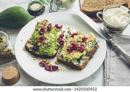 Healthy avocado toasts for breakfast or lunch with rye bread, cream cheese, arugula, sliced avocado, dried cranberry, pumpkin, hemp, sesame seeds, salt and pepper. Vegetarian sandwiches. Clean eating.