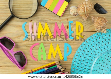 Text SUMMER CAMP of multicolored paper letters and sunglasses and hat on a natural wooden background. top view. flat lay