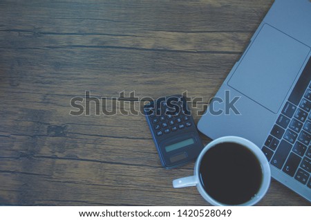 On the desk, the brown wood floor has a calculator and a notebook computer placed on it.White coffee cup on brown wood floor.Copy space.