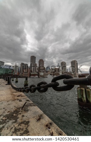 Chains in front of the Boston skyline at Fan Pier under cloudy skies.