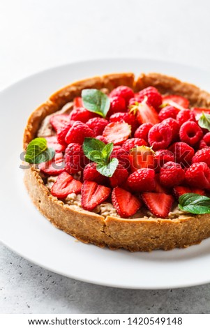 Vegan berry tart with raspberries, strawberries and cream on a white dish.