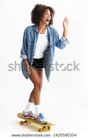 Full length portrait of a young cheerful african woman wearing casual denim clothes isolated over white background, riding on a skateboard