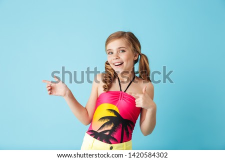 Cheerful little girl wearing swimsuit standing isolated over blue background, having fun