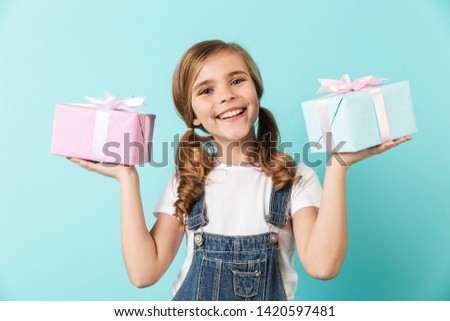 Portrait of a cheerful little girl isolated over blue background, showing present box