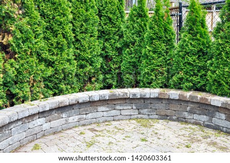 A functional retaining wall with coping adds seating at the edge of a tumbled paver patio and adjoining garden beds.