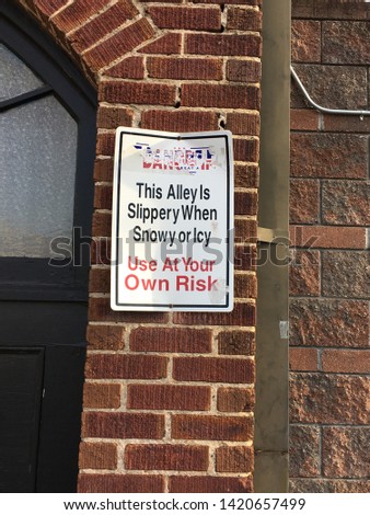 Sign on brick wall warning pedestrians that the sidewalk could be slippery when icy or snowy.  Rectangular sign in white with red and black lettering.