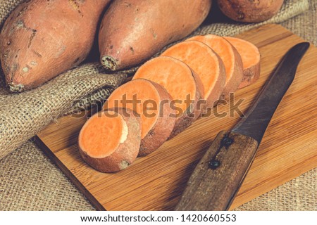 Sliced raw sweet potatoes on a wooden cutting board. Product photo of batats. Healthy diet for vegetarians and vegans. Source of vitamins. Wooden plank with batatas and knife