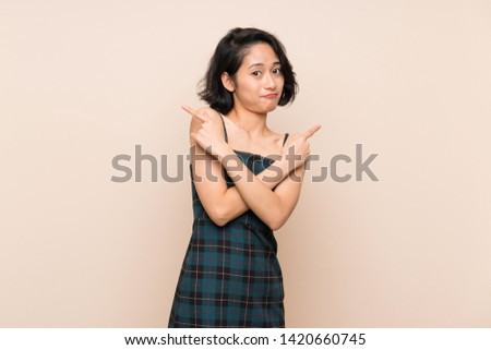 Asian young woman over isolated yellow wall pointing to the laterals having doubts