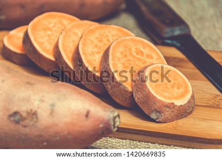 Sliced raw sweet potatoes on a wooden cutting board and jute backgroud. Product photo of batats. Healthy diet for vegetarians and vegans. Source of vitamins. Wooden plank with batatas and knife