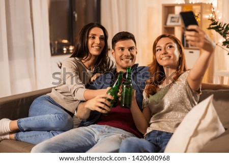 friendship and leisure concept - happy friends clinking drinks and taking selfie at home party in evening