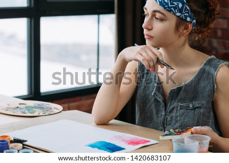 Creativity and imagination. Portrait of pensive female painter looking for inspiration. Blur window background.