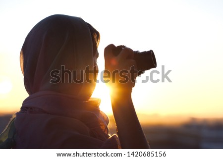 Arab Woman Photographer in a scarf taking picture using Camera on the sunset background. Halal travel concept 
