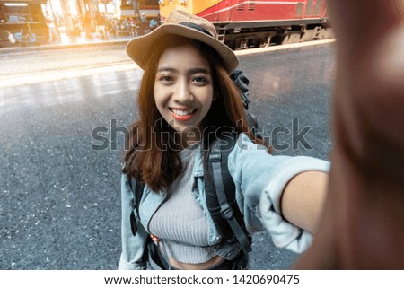 Attractive young Asian woman traveler with backpack taking a photo or selfie in train station. Travel lifestyle concept.