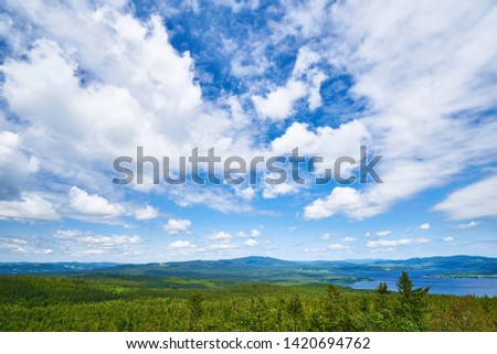 Blue sky with white clouds over the mountaneous landscape of Šumava nature preserve. View from lookout tower in castle ruins of Vítkův hrádek. The Lipno Reservoir in the background. Czech republic.