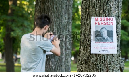 A young man puts up ads for a missing person in the park Royalty-Free Stock Photo #1420702205