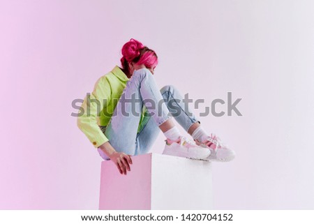 woman with pink hair sits on a cube light colored