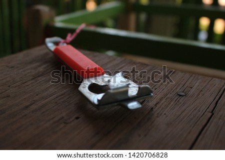 A red bottle opener placed on a brown wooden table in a restaurant. It is tied with a red rope attached to the table to prevent loss.Can use to open cans, open beer bottles, or open soda bottles