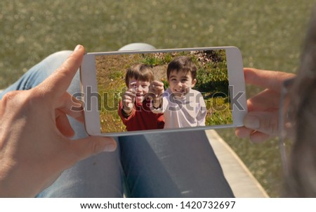 Human hands holding mobile looking at a picture of two twin children.