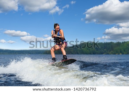 Young pretty slim brunette woman riding wakeboard on wave of motorboat in a summer lake Royalty-Free Stock Photo #1420736792